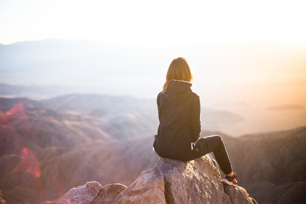 Woman sits on mountain edge looking at view.